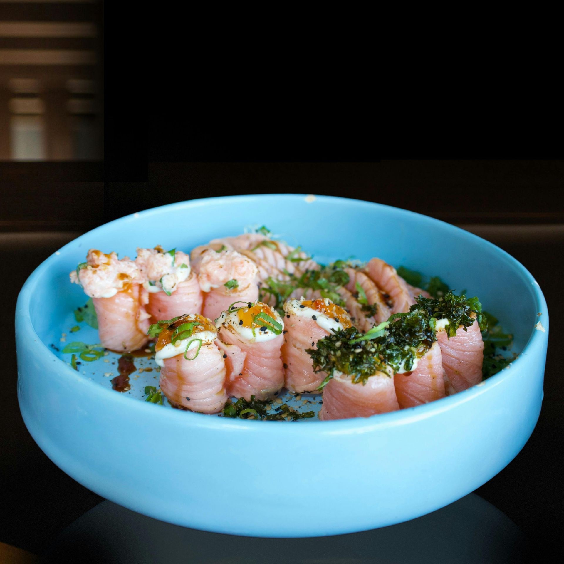 A plate of sushi rolls garnished with herbs and various toppings, served in a blue bowl.